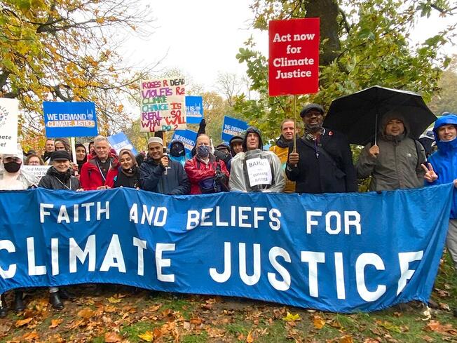 Pictures of various faith leaders standing in the rain holding a banner that says Faith and Beliefs for Climate Justice
